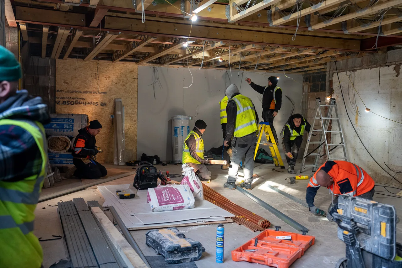 An installation team working together on ceiling services in a stripped-back interior