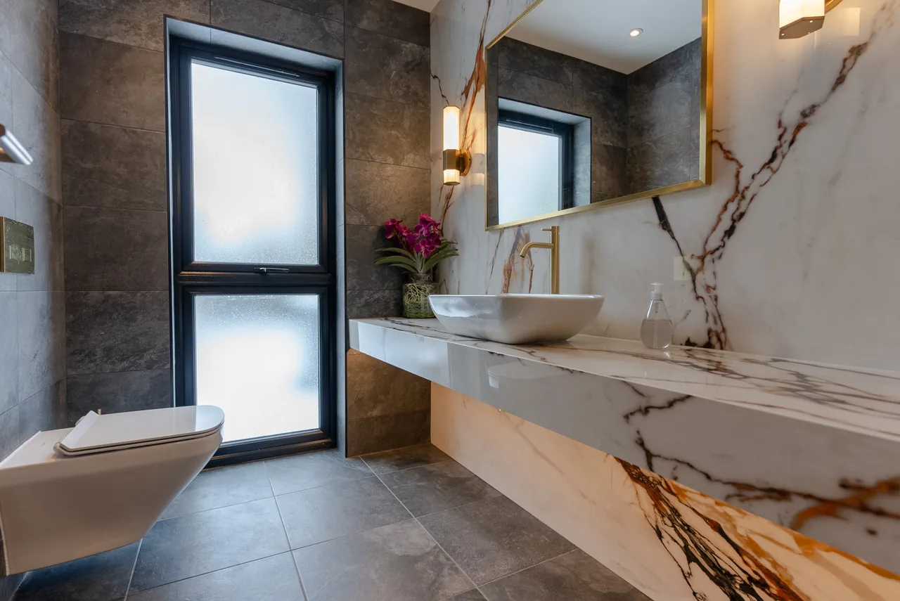 A marble bathroom with a backlit mirror and concealed strip lighting above the vanity