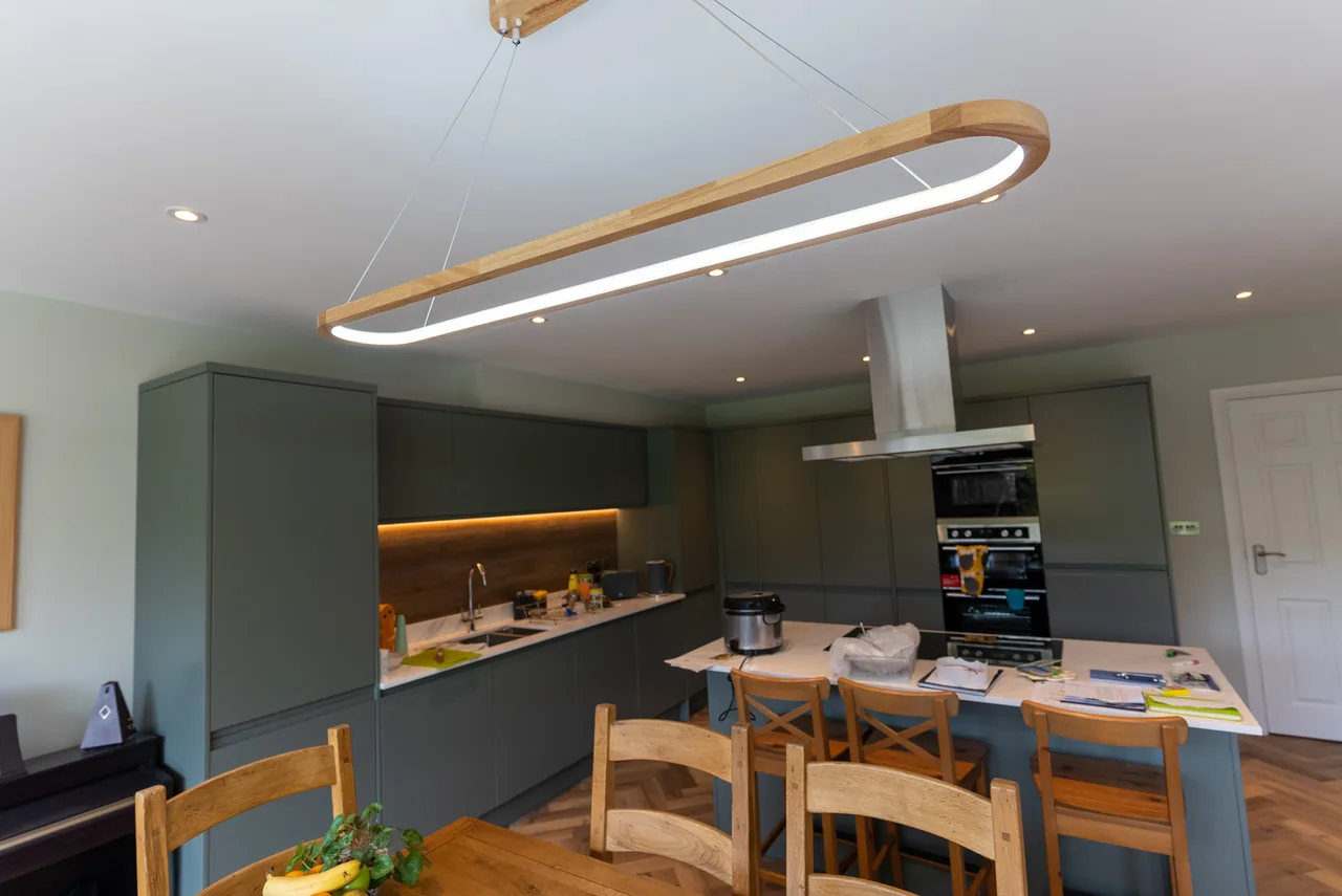 A kitchen with a linear suspended light over the island and lit undercabinet shelving