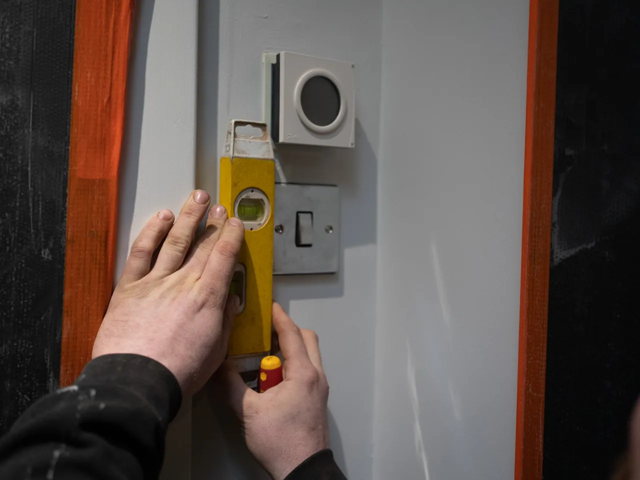 An engineer using a spirit level to set a wall-mounted control panel true